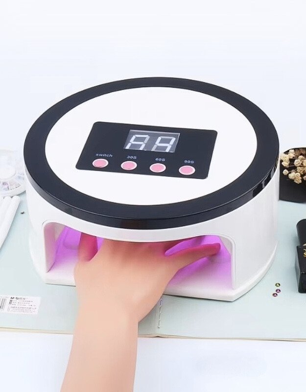 A professional LED nail lamp with a digital display and a hand placed inside for drying nails, featuring a white and pink color scheme.